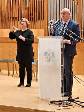 Minister Paweł Wdówik przemawia podczas Forum, przy mównicy na scenie, obok tłumacz języka migowego
