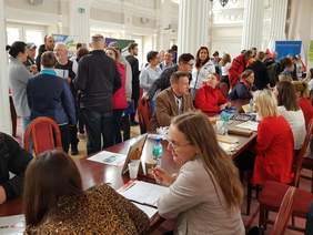 uczestnicy wydarzenia, tłum, część osób siedzi za stołami, inni stoją, rozmawiają