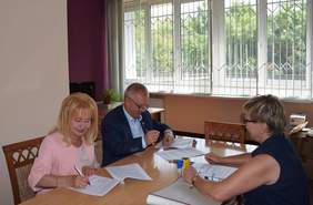 Pokaż zdjęcie: Trzy osoby siedzące przy stoliku podpisujące umowy