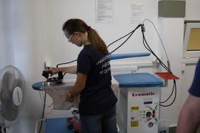 Mężczyzna stoi przy desce prasowalniczej, trzyma żelazko. 