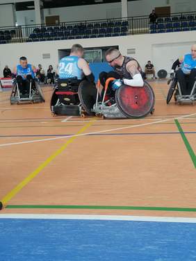 zdjęcie z rozgrywej, na pierwszym planie czterech zawodników nawózkach, w tle kilka osób widowni