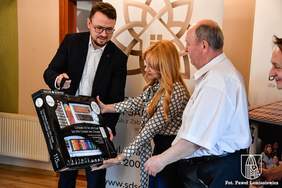 Pokaż zdjęcie: Dyrektor Oddziału wręcza laureatowi nagrodę, zestaw materiałów plastycznych w czarnym opakowaniu. 