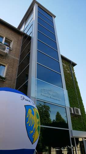 Pokaż zdjęcie: Widok na budynek Starostwa Powiatowego w Strzelcach Opolskich. Przy budynku widać dobudowany szyb windy