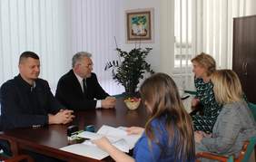 Pokaż zdjęcie: Dwóch mężczyzn i 3 kobiety siedzą  przy stole i rozmawiają. Jedna z kobiet trzyma kartki