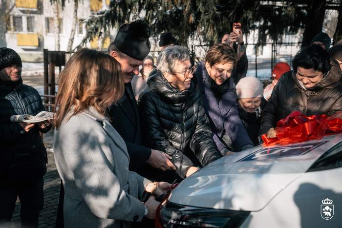Pokaż zdjęcie: Uroczyste przecięcie wstęgi przez sześć osób zebranych przy białym busie.