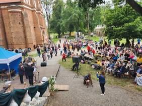 Pokaż zdjęcie: Z góry widok na uczestników festiwalu, część osób siedzi na ławkach, część spaceruje.