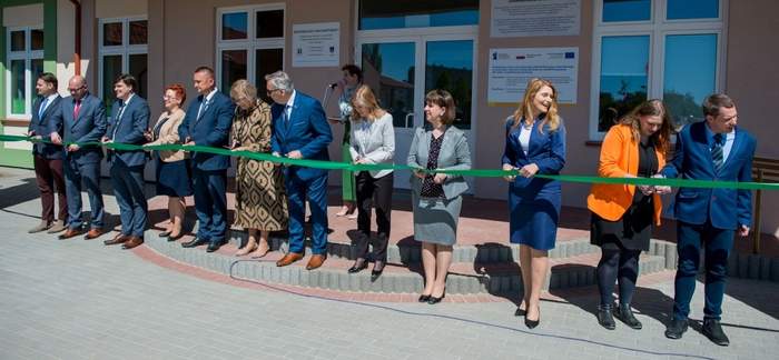 Pokaż zdjęcie: Na zdjęciu kilkanaście osób przecina wstęgę przed budynkiem