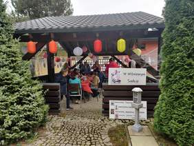 Pokaż zdjęcie: Warsztaty z rękodzieła przy jednej z sekcji. Widzimy uczestników przy stole wraz z prowadzącym. 