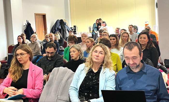 Uczestnicy spotkania siedzą na krzesłach podczas prelekcji