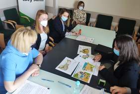 Pokaż zdjęcie: Goście siedzą przy stole w sali konferencyjnej, podpisują dokumenty. Na stole mapy z oznaczeniami oraz dokumenty