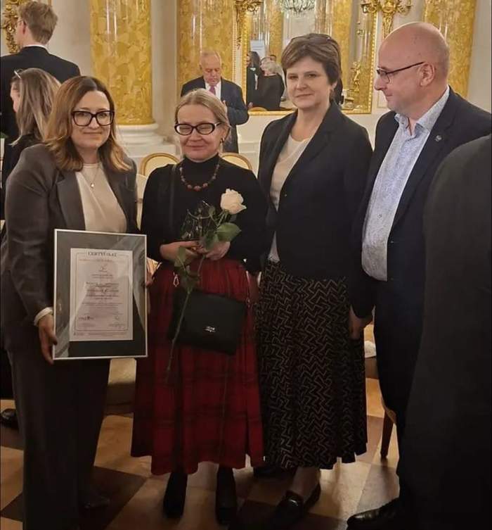 Pokaż zdjęcie: Trzy kobiety i mężczyzna pozują z laureatką lodołamacza. Kobieta z lewej trzyma dyplom w ręku. Laureata stoi obok z różą w ręku.