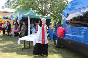 Pokaż zdjęcie: Ksiądz święci granatowego busa z czerwoną kokardą
