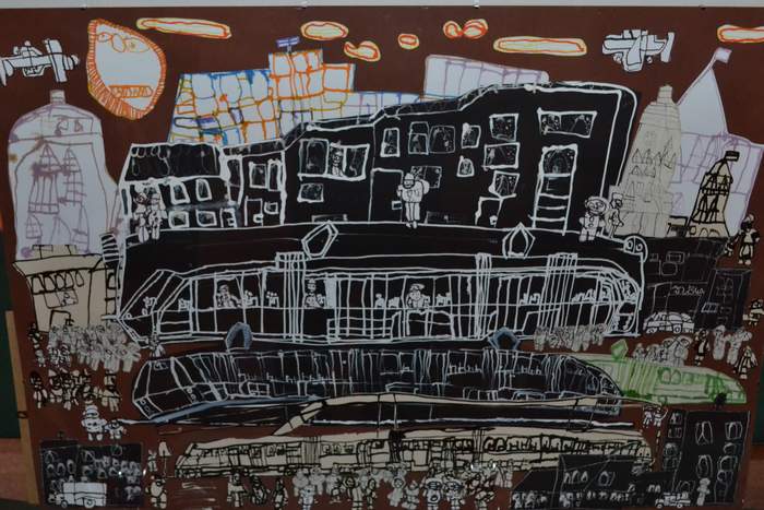 Pokaż zdjęcie: Rysunek w tonacji brązowo, czarno-zielonej. Widać przystanek pełen ludzi, tramwaj i otaczające budynki oraz kawałek zieleni miejskiej