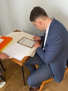 Pokaż zdjęcie: Mężczyzna siedzi przy stole i podpisuje dyplomy i wyróżnienia