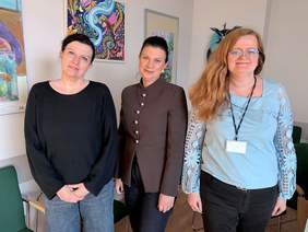 Pokaż zdjęcie: Trzy uśmiechnięte kobiety pozują do zdjęcia. W tle na ścianie widoczne fragmenty obrazów.