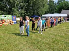 zielona trawa, zielone drzewa, słoneczny dzień kilkanaście osób idą parami