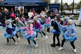 Pokaż zdjęcie: Zdjęcie na zewnątrz grupy przedszkolaków podczas występu artystycznego. Dzieci tańczą.