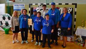 Pokaż zdjęcie: 9 osób na hali gimnastycznej, 6 z nich ubrana w niebieskie koszulki z medalami na szyi