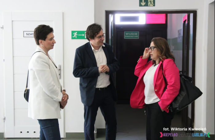 Pokaż zdjęcie: Przed wejściem do warsztatu stoją dwie kobiety i mężczyzna, rozmawiają.