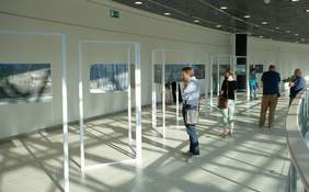 Pokaż zdjęcie: W Centrum Handlowym grupa osób ogląda wystawę fotografii 