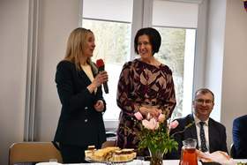 Przy świątecznym stole stoją dwie kobiety. Jedna z nich trzyma w ręku mikrofon.