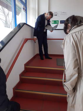 Pokaż zdjęcie: Oględziny i pomiary klatki schodowej, ekspert  BHP mierzy wysokość poręczy, druga osoba ocenia powierzchnię antypoślizgową
