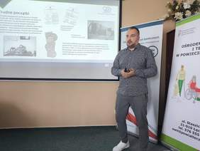 Pokaż zdjęcie: Mężczyzna w swetrze prowadzi wykład w sali konferencyjnej.