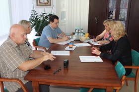 Zdjęcie pokoju w biurze, przy stole siedzi pięć osób, na stole leżą dokumenty 