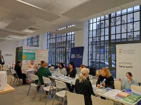 Pokaż zdjęcie: na zdjęciu sala obsługi klientów w Narodowym Funduszu Zdrowia po prawej stronie ustawione są stanowiska z logo instytucji PFRON , ZUS, Fundacja Aktywizacja i inne na stanowiskach siedzą osoby i udzielają porady siedzącym po drugiej stronie stanowis