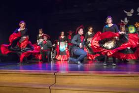 Pokaż zdjęcie: Na scenie grupa taneczna w czarnoczerwonych strojach.