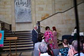 Pokaż zdjęcie: Kobieta w drugiej kolorowej sukience odbiera nagrodę z rąk prezesa PFRON