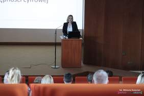 Pokaż zdjęcie: Na scenie przy mównicy stoi kobieta w granatowym garniturze