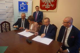 Pokaż zdjęcie: Cztery osoby siedzą przy stole i podpisuja dokumenty