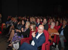 Pokaż zdjęcie: sala widowiskowa na której siedzą widzowie i oglądają występy artystyczne oraz teledyski