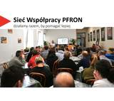 Sala wypełniona dorosłymi uczestnikami siedzącymi przy stołach, zwróconymi w stronę prowadzącego. Prelegent stoi z przodu z mikrofonem w dłoni, obok ekranu z wyświetloną prezentacją. W tle widać rośliny doniczkowe, drzwi oraz ściany ozdobione oprawionymi fotografiami. W lewym górnym rogu widnieje hasło „Sieć Współpracy PFRON – działamy razem, by pomagać lepiej”.