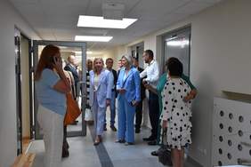 Pokaż zdjęcie: Zdjęcie korytarza, grupa osób zwiedza zaglądając do poszczególnych sal lekcyjnych.