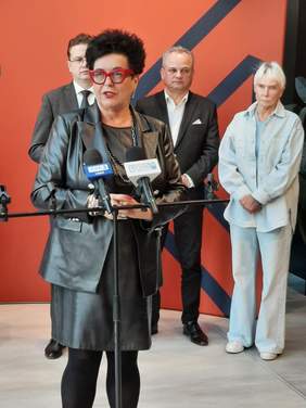 Pokaż zdjęcie: Przy mikrofonie stoi pani Bożena Borowiec – Zastępca Prezesa Zarządu ds. Programowych PFRON. Trwa konferencja prasowa. W tle widać inne osoby. 