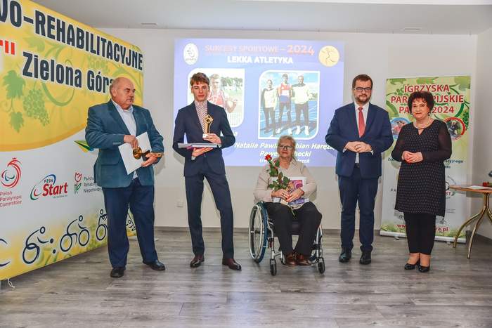 Pokaż zdjęcie: Na tle banerów "Start" Zielona Góra stoją obok siebie Dyrektor Oddziału Lubuskiego PFRON, Prezes "Start" Zielona Góra wraz z uhonorowanymi sportowcami i działaczami