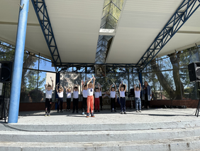 Pokaż zdjęcie: Na scenie stoi kilkoro dzieci trzymających w rękach grzechotki ku Górze. Za nimi obraz Matki Boskiej trzymającej Jezuska.