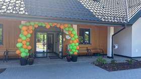 Wejście do budynku ozdobione zielono-pomarańczowym łukiem z balonów podczas uroczystości otwarcia.