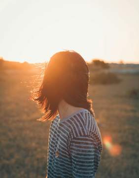 Pokaż zdjęcie: Na pierwszym planie znajduje się człowiek, który patrzy w stronę wschodzącego słońca. Za nim jest krajobraz. Widać widnokrąg, roślinność i wschodzące słońce. 