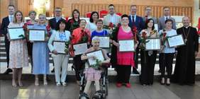 Pokaż zdjęcie: W kościele przed ołtarzem stoją ludzie. Trzymają w rękach dyplomy z napisem: Tytuł "Człowiek o godnym sercu". Są elegancko ubrani i uśmiechają się. 