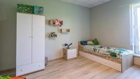 Pokaż zdjęcie: Pokój dziecięcy z niskim pojedynczym łóżkiem, białą szafą oraz półkami na ścianie