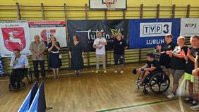 Pokaż zdjęcie: W hali sportowej trwa uroczyste otwarcie, zdjęcie grupy osób, w tym część osób jest na wózkach inwalidzkich. 