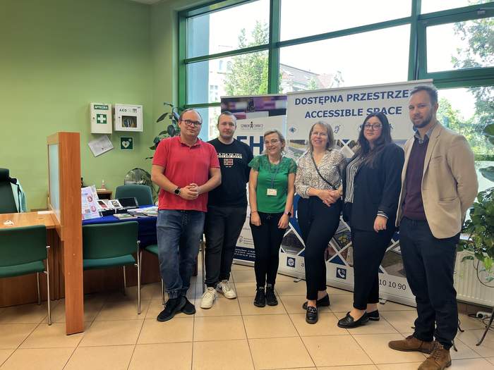 Pokaż zdjęcie: Grupa osób, kobiet i mężczyzn, stoi obok siebie w budynku ZUS, są uśmiechnięci, ubrani zwyczajnie