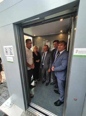 Pokaż zdjęcie: na zdjęciu zewnętrzna winda w której stoi kilka osób i testuje przejazd windą