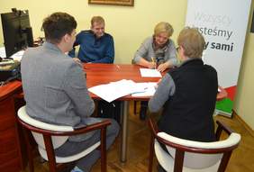 Pokaż zdjęcie: Na zdjęciu 2 kobiety i 2 mężczyzn siedzą przy stole i podpisują umowy