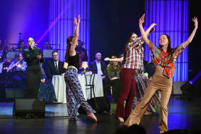 Kobiety w kolorowych strojach w stylu lat siedemdziesiątych, w tanecznej pozie, na scenie