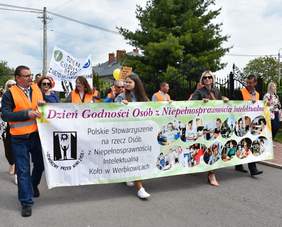 Pokaż zdjęcie: Początek korowodu, osoby trzymają baner z napisem Dzień Godności Osób z Niepełnosprawnością Intelektualną.