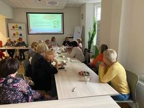 Na sali przy stołach siedzą przedstawiciele PFRON i seniorzy, w tle widoczna prezentacja